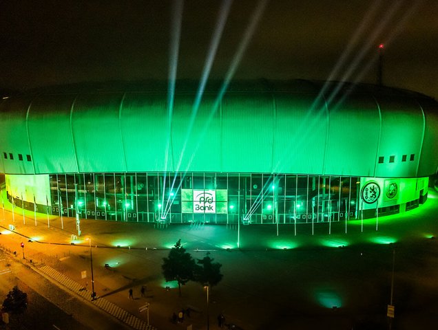 Außenansicht PSD BANK DOME grün beleuchtet. In der Mitte sieht man das Logo der PSD BANK, rechts und links davon gehen grüne Lichtkegel in die Luft.