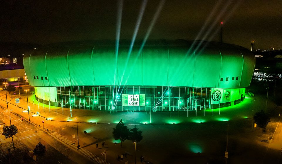 Exterior view of PSD BANK DOME illuminated in green. The PSD BANK logo is visible in the middle, to the right and left green cones of light are shining up in the air.